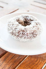 Piece of chocolate coconut donut on white plate