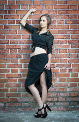 Fototapeta na wymiar Charming young brunette woman in black dress near brick wall