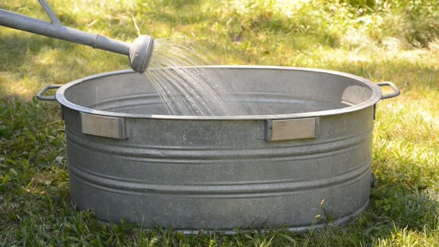 Zinkbadewanne im Garten durch eine Gießkanne wird sie mit Wasser gefüllt