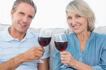 Couple toasting with red wine on the sofa smiling at camera