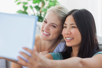 Two pretty friends taking photo with tablet pc