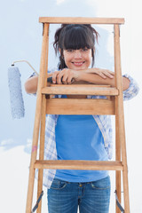 Happy woman holding paint roller leaning on ladder