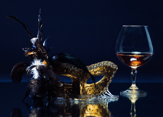 mask with feather and brandy on a mirror table