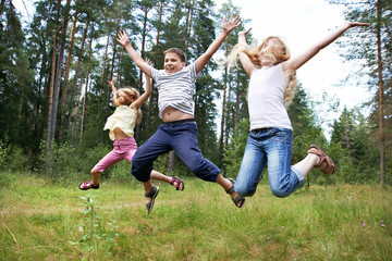 Naklejka na ściany i meble Children jump on lawn in summer forest