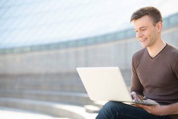 Working outdoors. Cheerful young man working on laptop outdoors