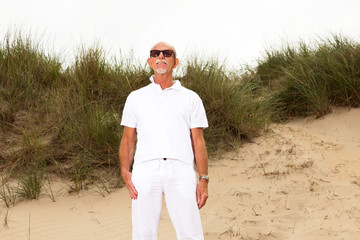 Retired man with beard and sunglasses in grass dune landscape wi