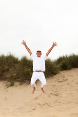 Fototapeta na wymiar Jumping happy retired man with beard and sunglasses in grass dun