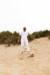 Retired man with beard and sunglasses walking in grass dune land