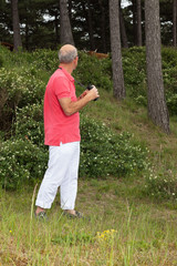 Senior man using binoculars outdoors. Watching scottish highland