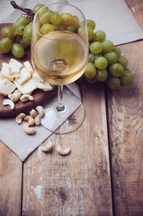 glass of white wine, grapes, cashew nuts and soft cheese