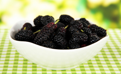 Ripe mulberries in bowl on table on bright background