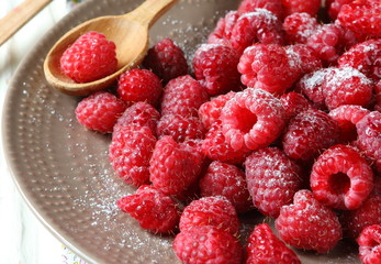 juicy raspberries on a plate and wooden spoon