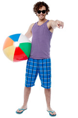 Cheerful guy with beach ball pointing at you