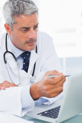 Naklejka na ściany i meble Focused doctor watching something on his laptop