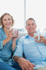 Happy middle aged couple sitting on the couch having coffee