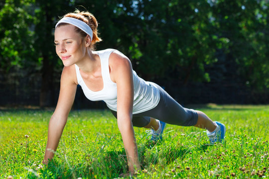 Young woman doing push ups on green grass.