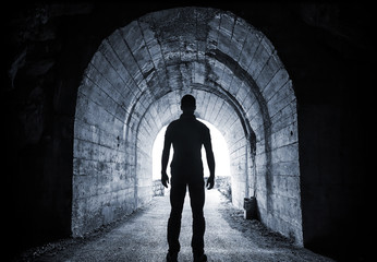 Man stands in dark tunnel and looks in glowing end - Powered by Adobe