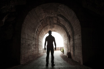 Young man stands in dark tunnel and looks out