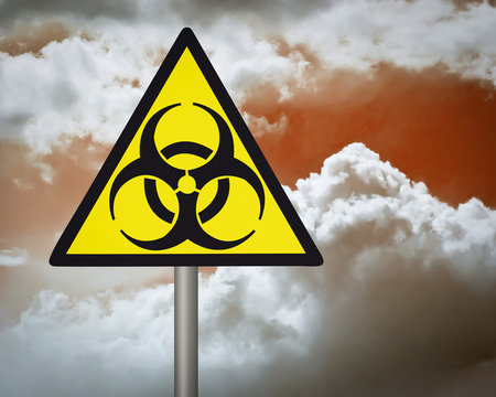 Yellow biohazard warning sign on against dark cloudy sky.