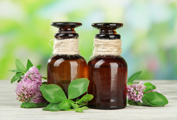 Medicine bottles with clover flowers on wooden table, outdoors