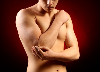 Young man with elbow pain, on red background