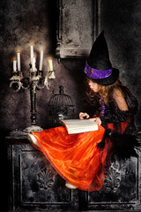 Little girl witch with a book in her hands and candles on hallow