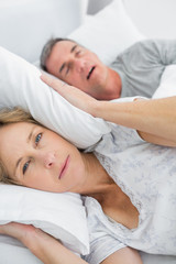 Fototapeta na wymiar Tired wife blocking her ears from noise of husband snoring looki