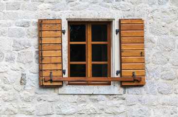 Wooden window with open jalousies in old gray stone wall