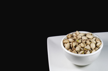 Bowl of pistachios on white plate.