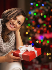 Portrait of smiling young woman near christmas tree holding gift