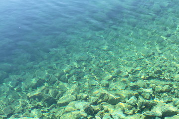 Naklejka na ściany i meble Sea water with sunlight on turquoise pebbles background