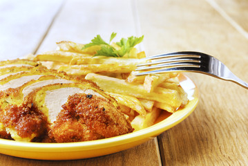 French fries and chicken on the plate on the wooden table