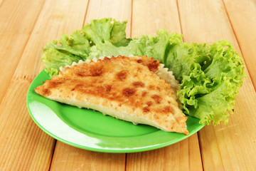 Tasty chebureks with fresh herbs on plate,on wooden background