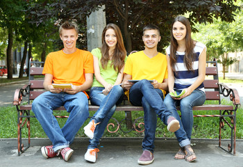 Happy group of young students sitting in park