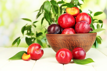 Ripe plums in bowl on wooden table on natural background
