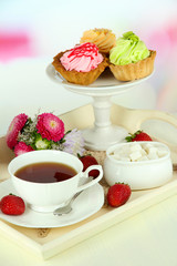 Cup of tea with cakes on wooden tray on table in room