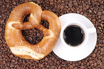 Tasse Kaffee mit Laugenbrezel und Kaffeebohnen