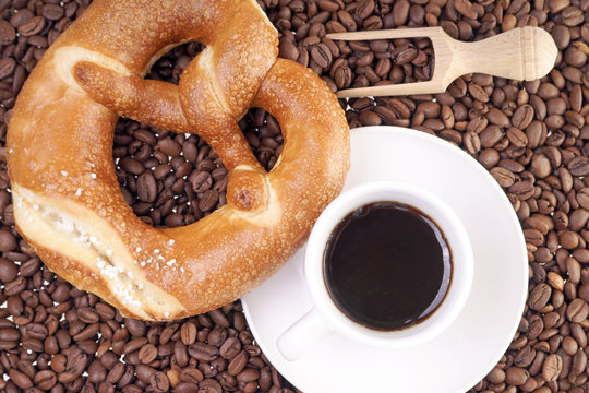 Tasse Kaffee mit Laugenbrezel und Kaffeebohnen