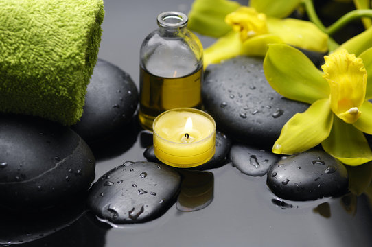 bottle of essential oil with two orchid and candle on pebbles