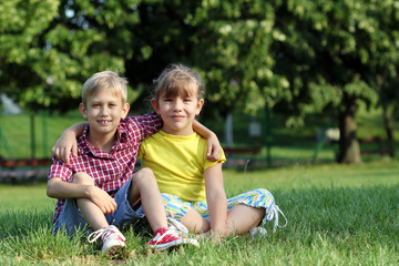 Naklejka na ściany i meble happy little girl and boy sitting on grass