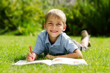 Portrait of a boy lying on the grass with a book in the park