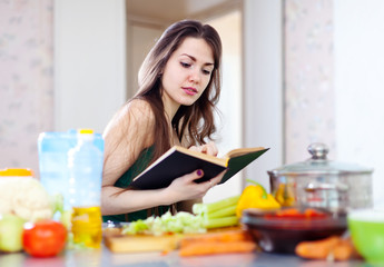 Obraz na płótnie Canvas beautiful housewife cooking with cookbook