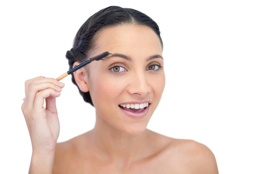 Surprised young brunette using eyebrow brush