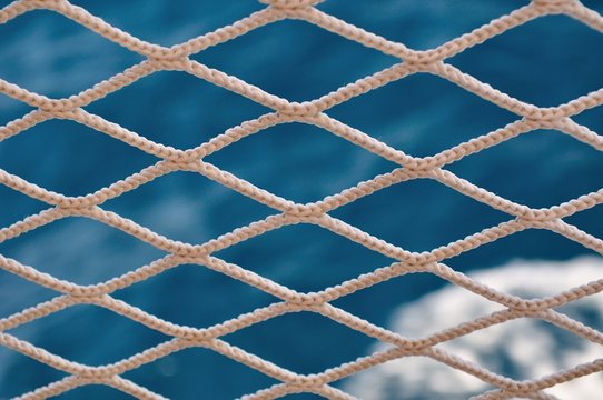 Knitted grid on boat banister with blurred sea on background