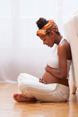 Young pregnant black woman touching her belly - African people