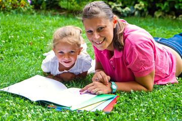 happy mother drawing a book with baby girl in garden