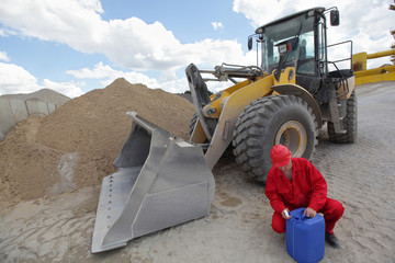 driver in uniform checking petrol can, bulldozer in background © endostock