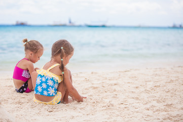 Two little sisters in nice swimsuits playing on sandy beach