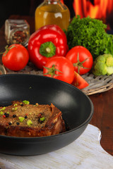 Piece of fried meat on pan on wooden table on fire background