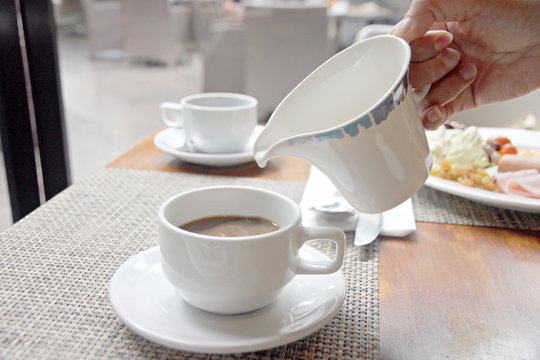 Pouring milk into coffee cup.
